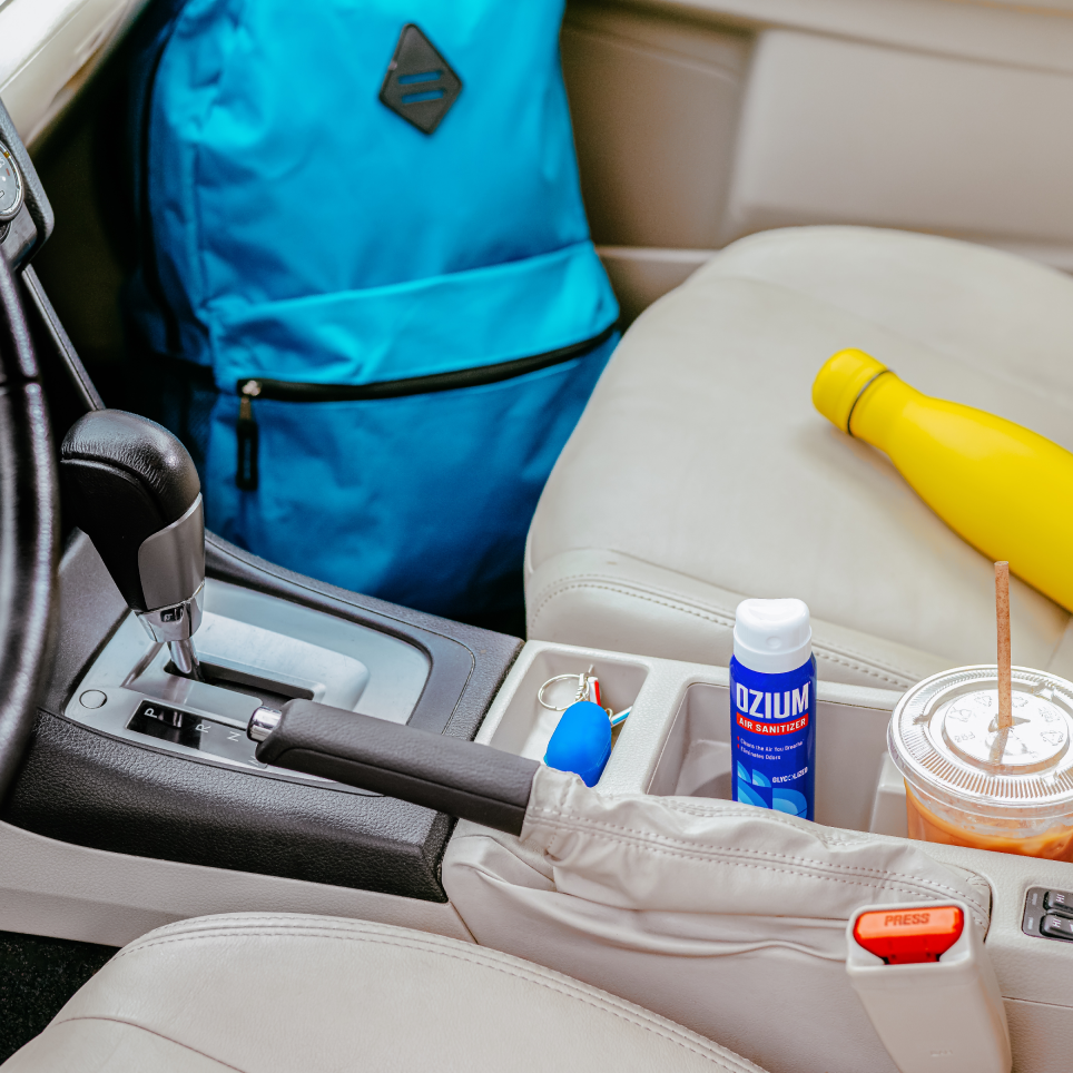 Ozium air sanitizer featured in a car next to a backpack
